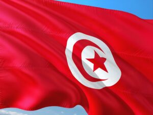 Bandiera della Tunisia con fondo rosso, raffigurante una mezzaluna bianca e una stella rossa al centro, vibrante sotto il cielo azzurro.