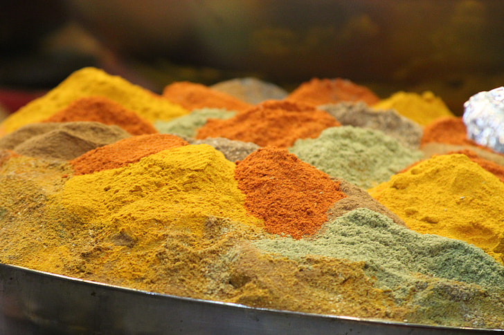 Monticelli di spezie colorate in un mercato, con tonalità di giallo, arancione, rosso e verde, che richiamano i sapori della cucina tunisina.