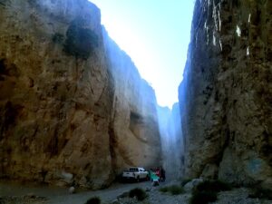 Gole rocciose con pareti verticali strette illuminate dall’alto, strada sterrata e un pick-up parcheggiato in fondo al canyon.