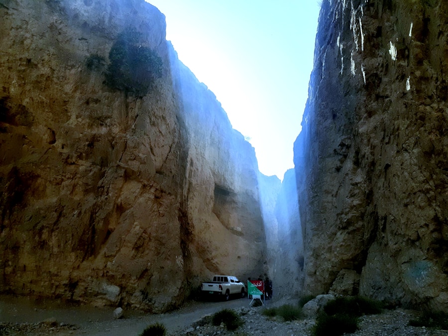 Gole rocciose con pareti verticali strette illuminate dall’alto, strada sterrata e un pick-up parcheggiato in fondo al canyon.