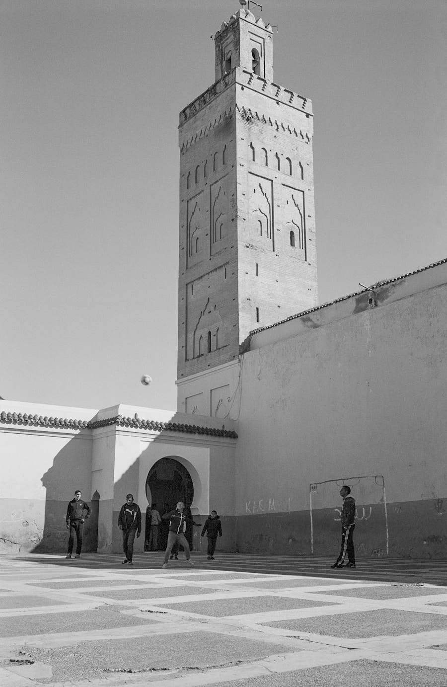 Minareto storico a Marrakech con persone che giocano a calcio in un cortile. Scena di vita quotidiana marocchina.
