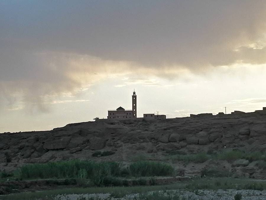 Moschea isolata nel deserto al tramonto, con minareto visibile, cielo nuvoloso e paesaggio roccioso