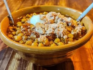 Zuppa di lablabi con ceci con tonno sminuzzato, uovo in camicia e spezie servita in ciotola di terracotta.