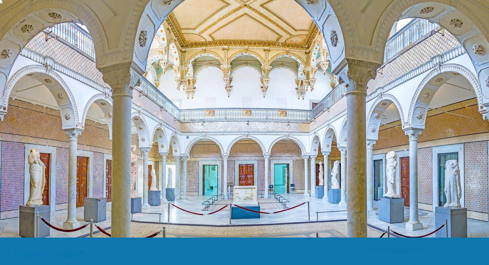 Interno di museo luminoso con colonnato ad archi, balconata superiore e statue marmoree lungo le pareti, sala espositiva centrale